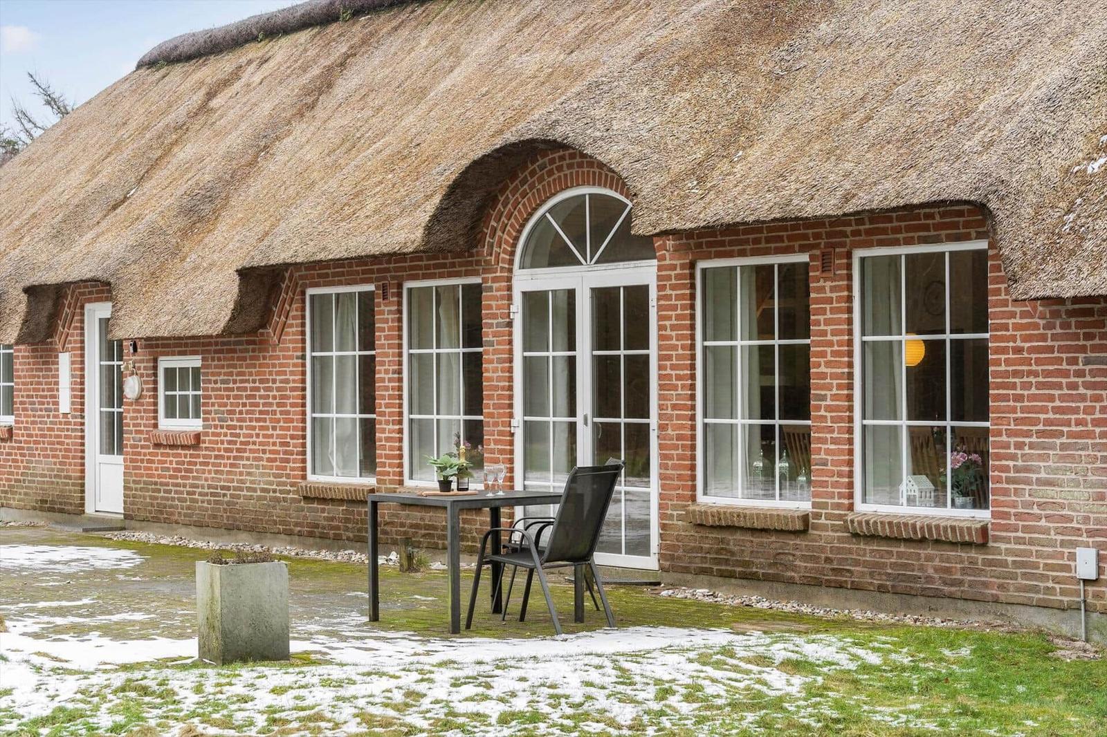 Haus mit Strohdach, Backsteinfassade und Fenstern. Außenbereich mit Tisch und Stuhl.