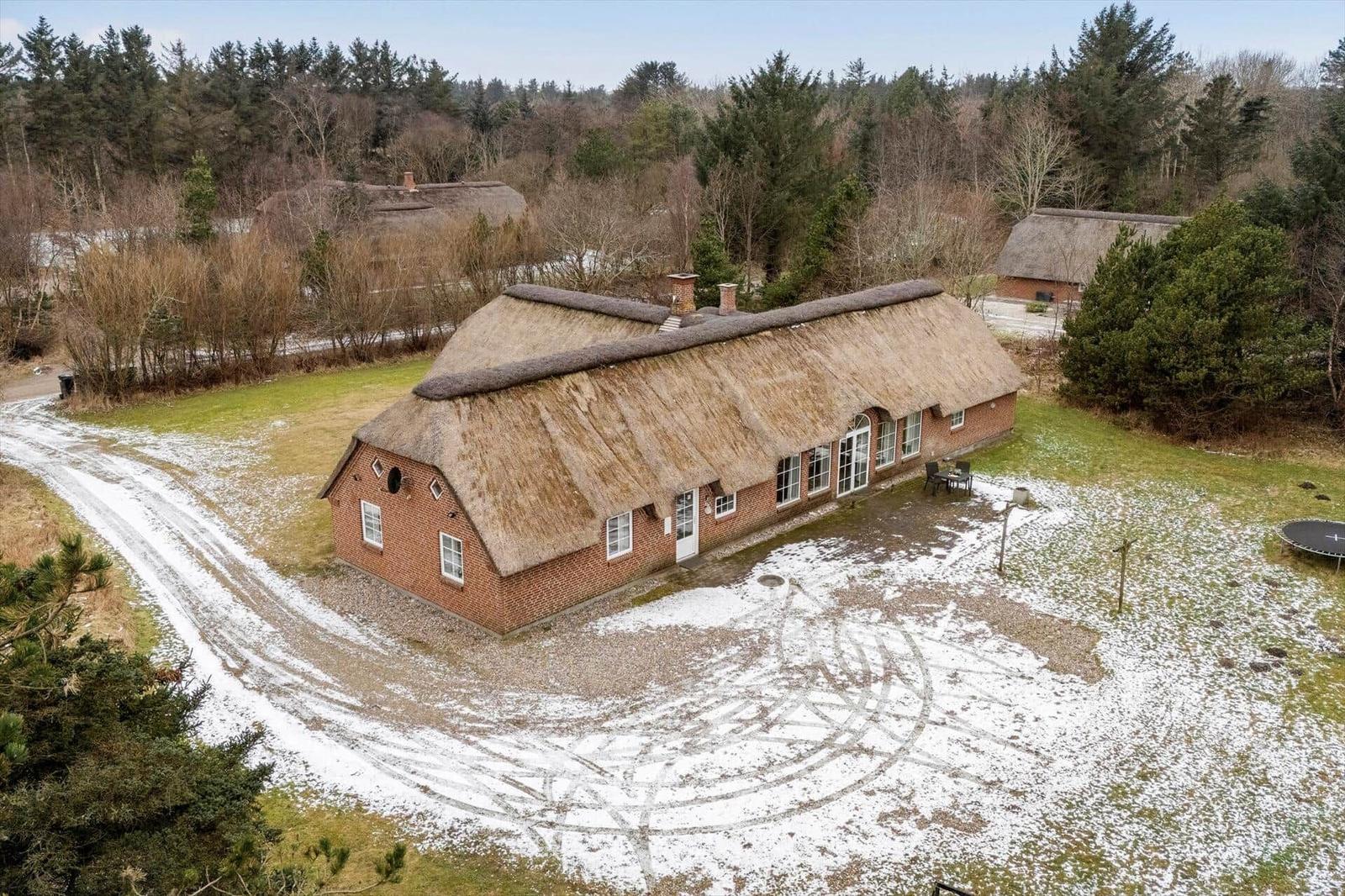 Rotes Backsteinhaus mit Strohdach, umgeben von Wald und Schnee.