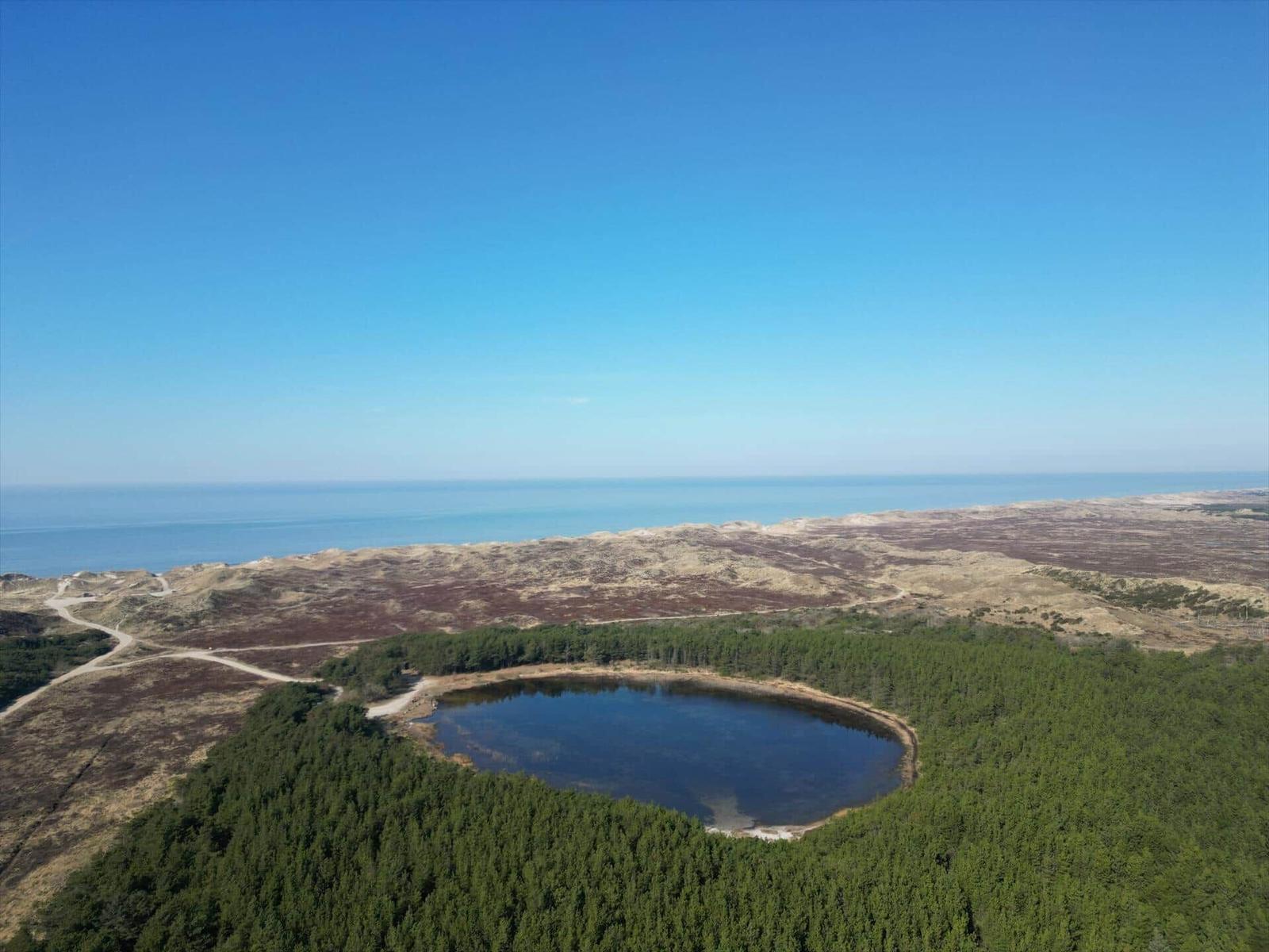 Ein kreisförmiger See liegt inmitten von Wäldern, umgeben von Hügeln und dem Meer.