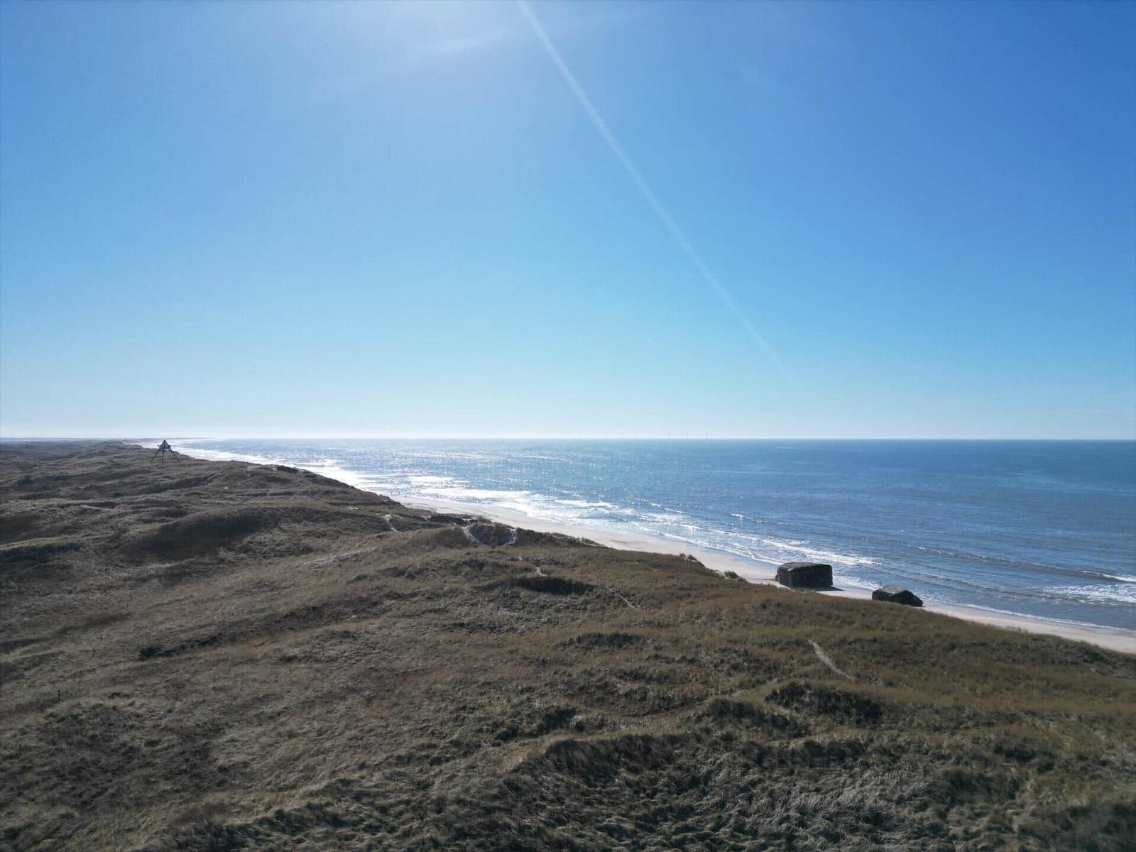 Meer und Strand aus der Dünenlandschaft mit klarem Himmel.