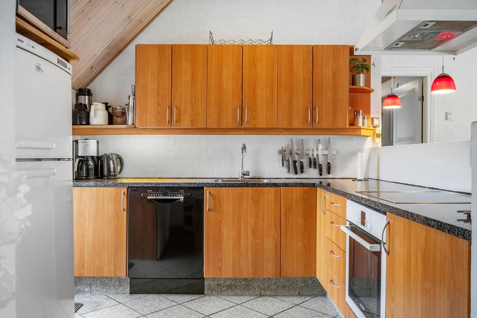 Küche mit Holzschränken, Spüle und Kochfeld. Geräte wie Kühlschrank und Mikrowelle vorhanden.