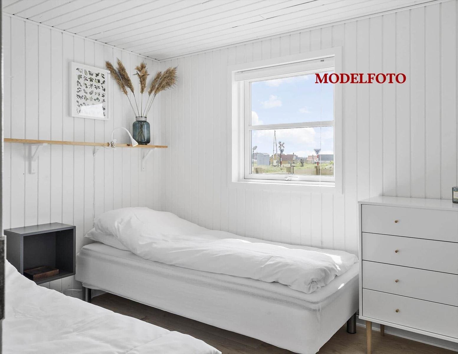 Schlafzimmer mit weißem Bett, Schrank und Fensterblick.