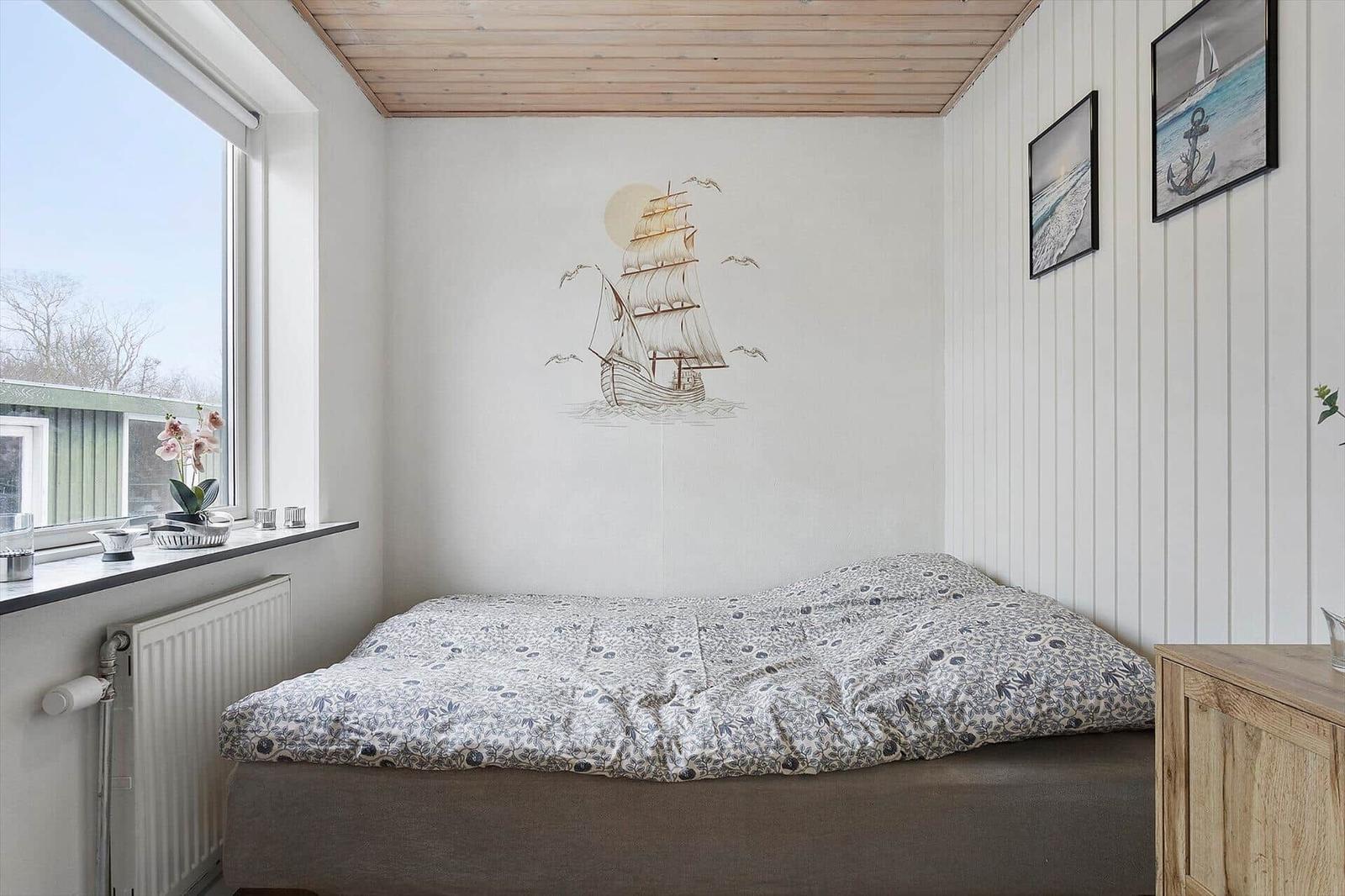 Bedroom with bed, window, and wall mural of a sailing ship.
