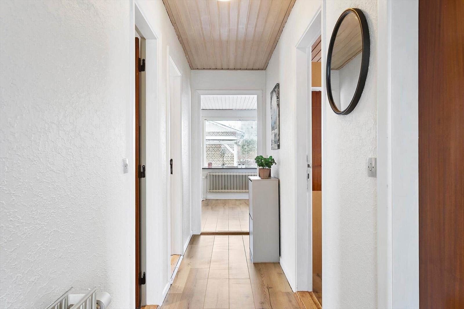 Hallway with wooden floor, white walls, and round mirror on the wall.