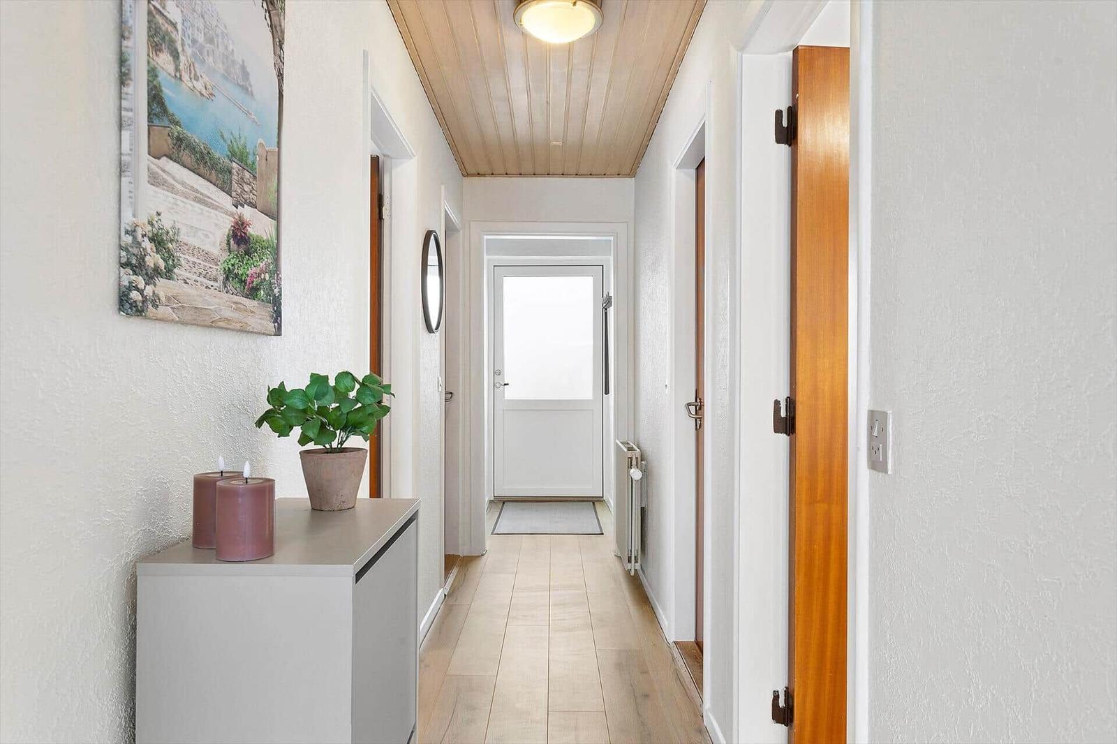 Hallway with wooden floor, white walls, and a door to the outside.