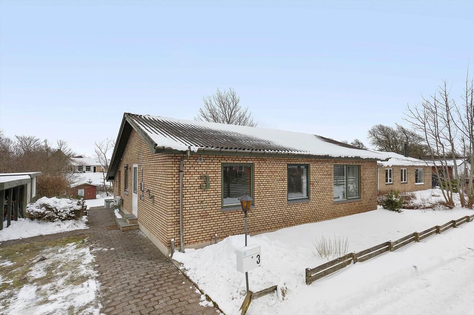 Single-story house with snow-covered roof and stone path.