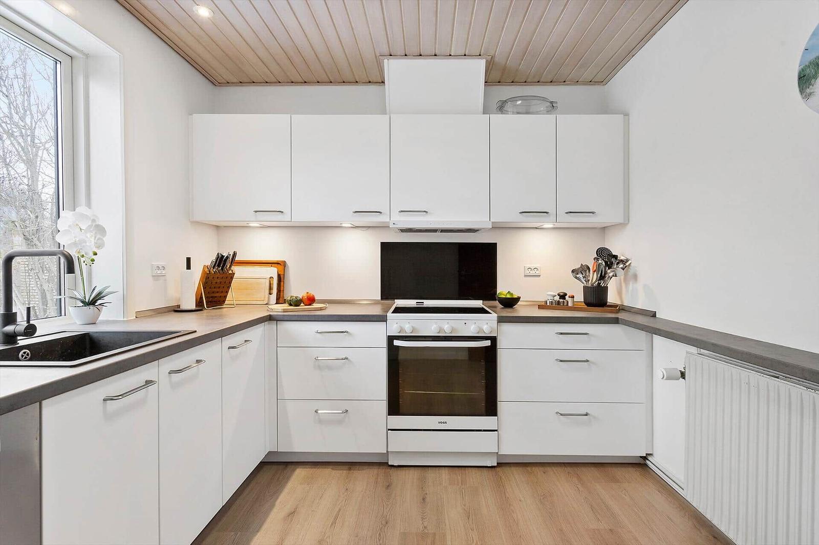 Modern kitchen with white cabinets, dark worktop, and wooden floor.
