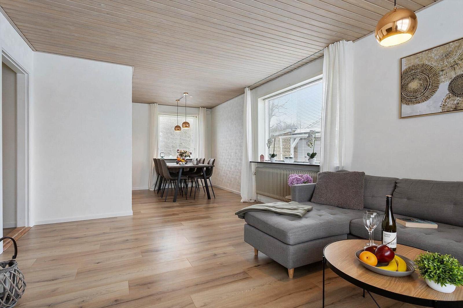 Living and dining area with wooden floor, gray sofa, and dining set.