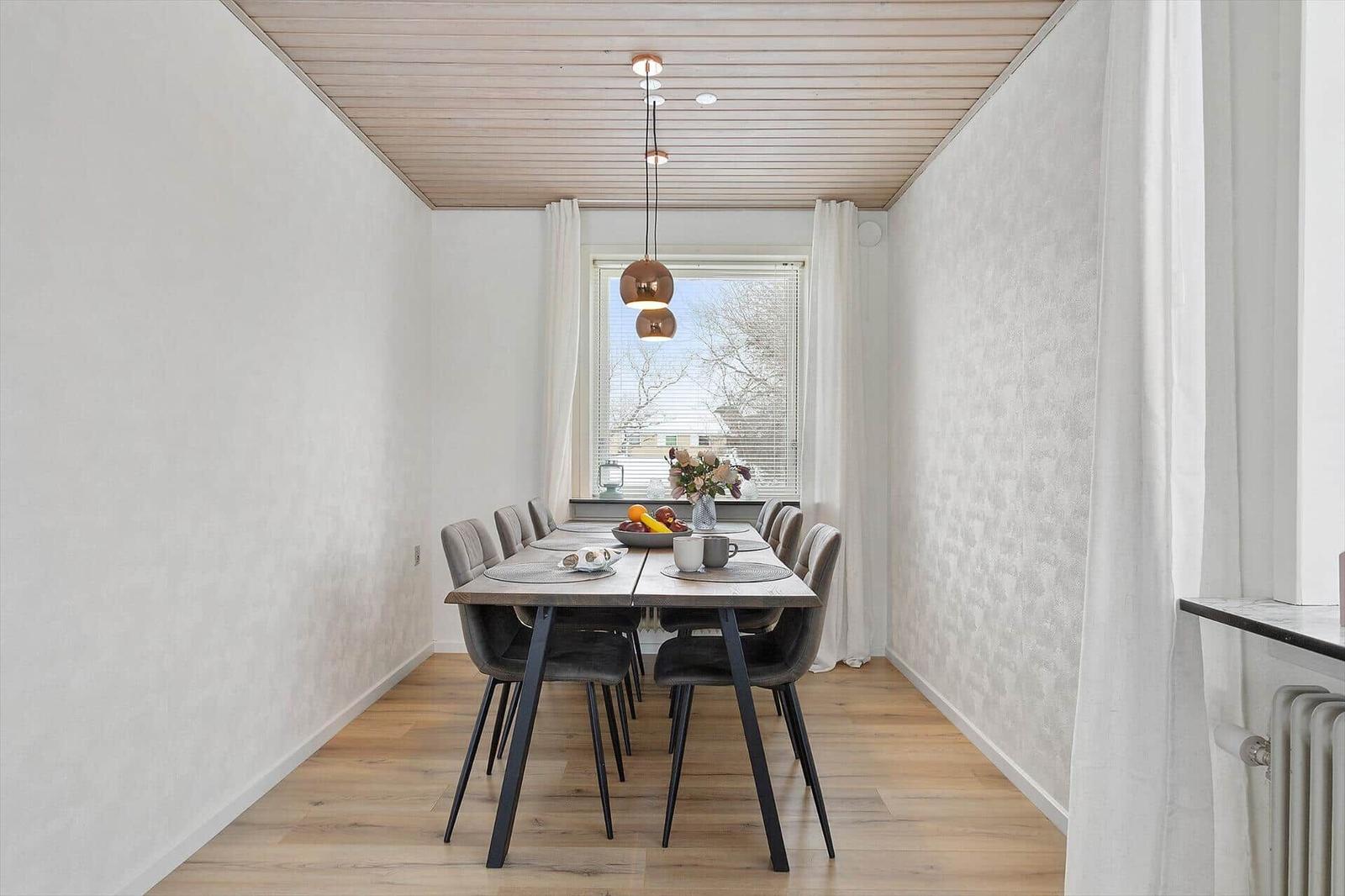 Dining room with long table, chairs, and window with curtains.