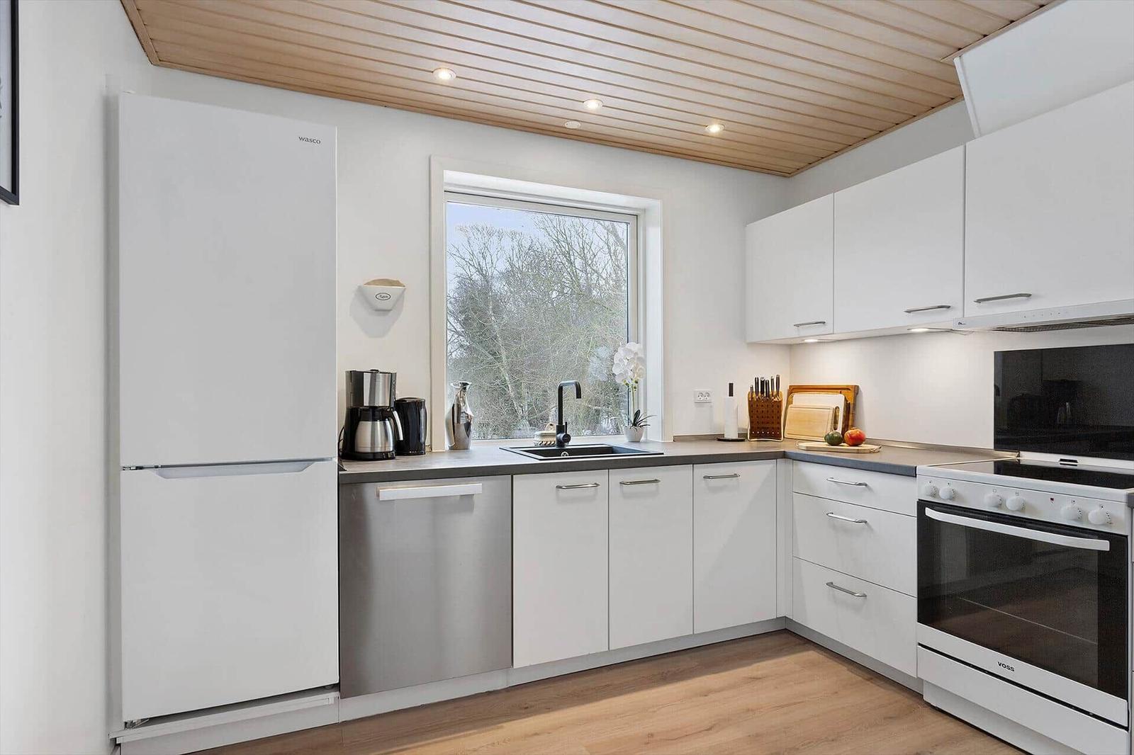 Modern kitchen with white cabinetry, window, and wooden floor.