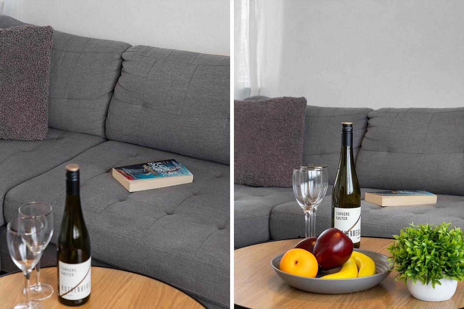 Gray sofa with cushions, table with wine, fruit, and plant.