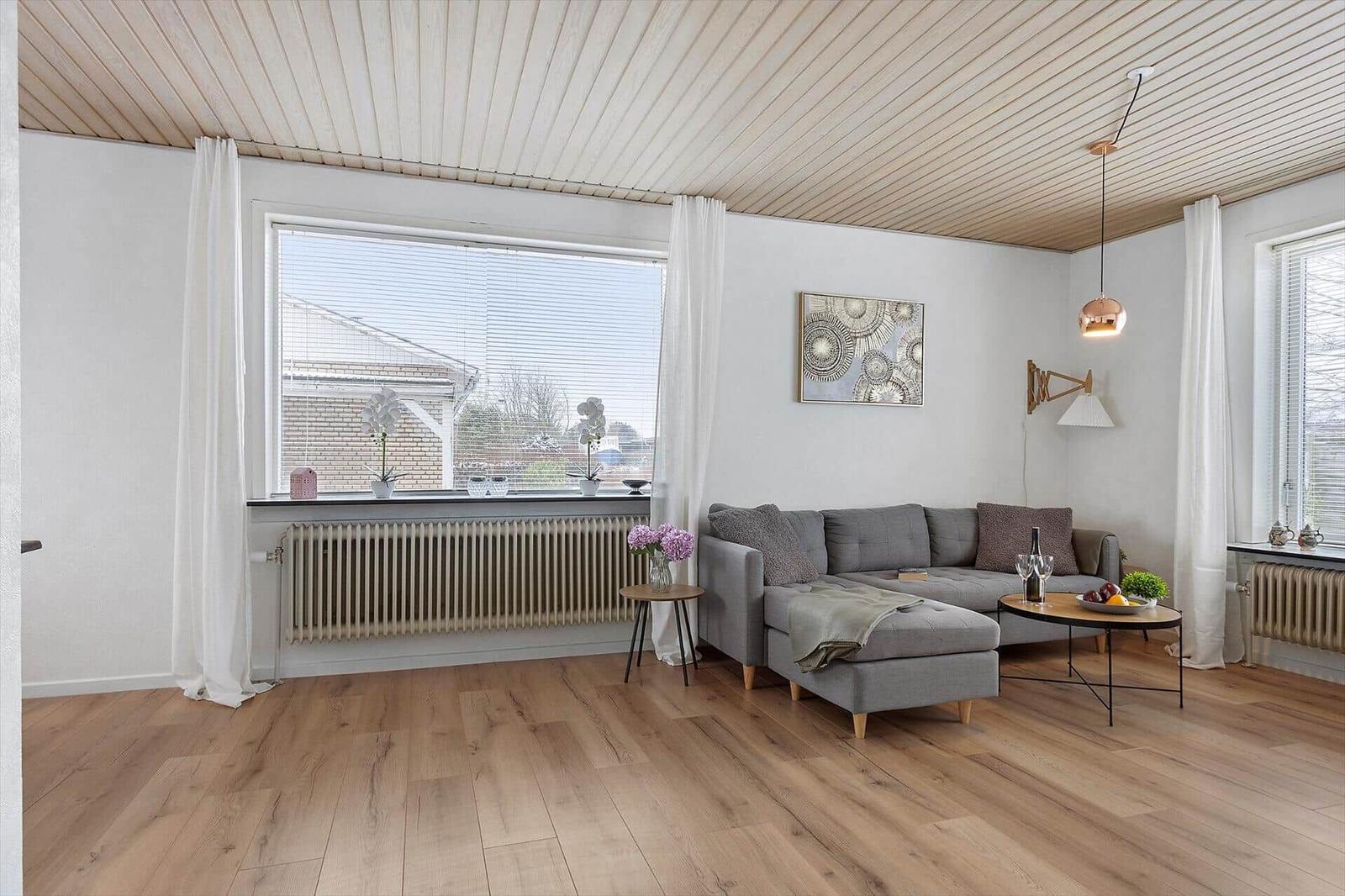 Living room with gray sofa, wooden floor, and large windows.