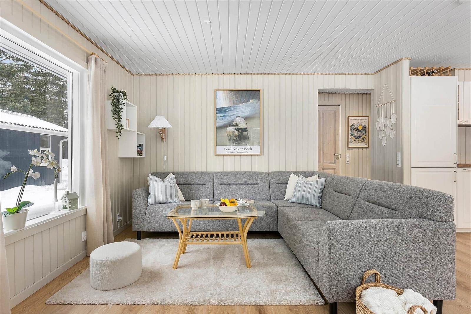 Living room with gray sofa, glass table, and wooden floor. A picture hangs on the wall.