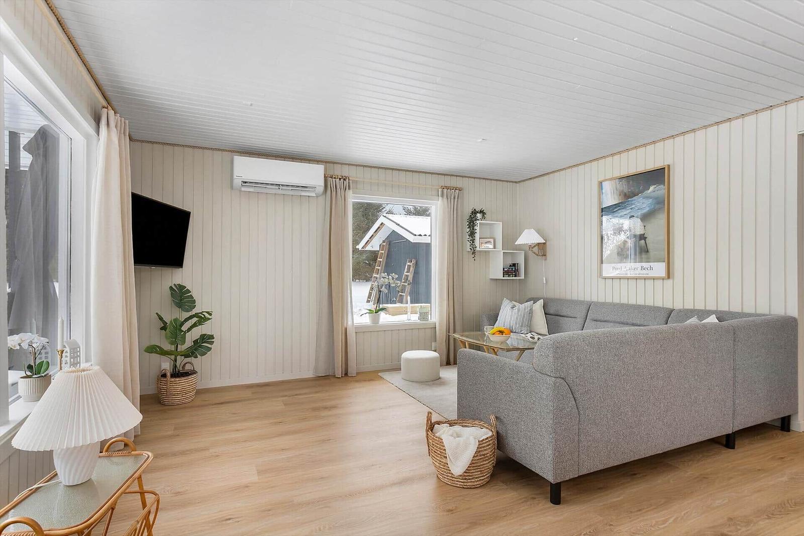 Living room with gray sofa, wooden floor, and white walls. Windows with view outside.