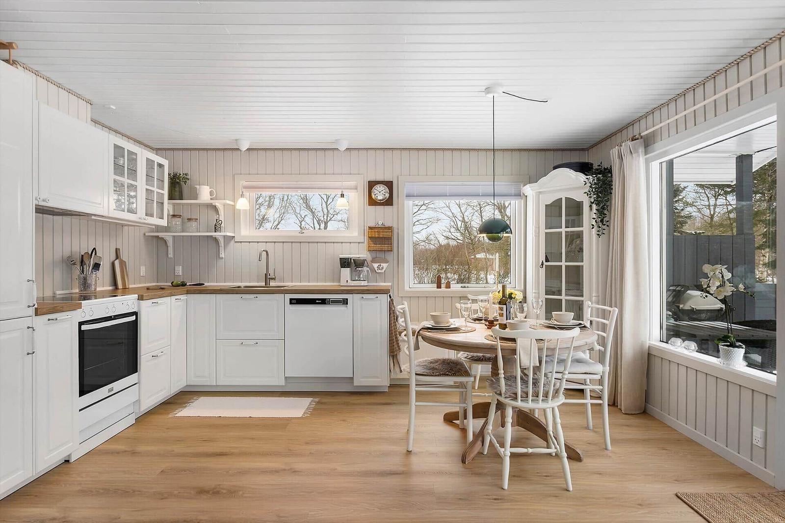 Kitchen with dining area, white cabinets, and wooden floor. Table with chairs and windows.