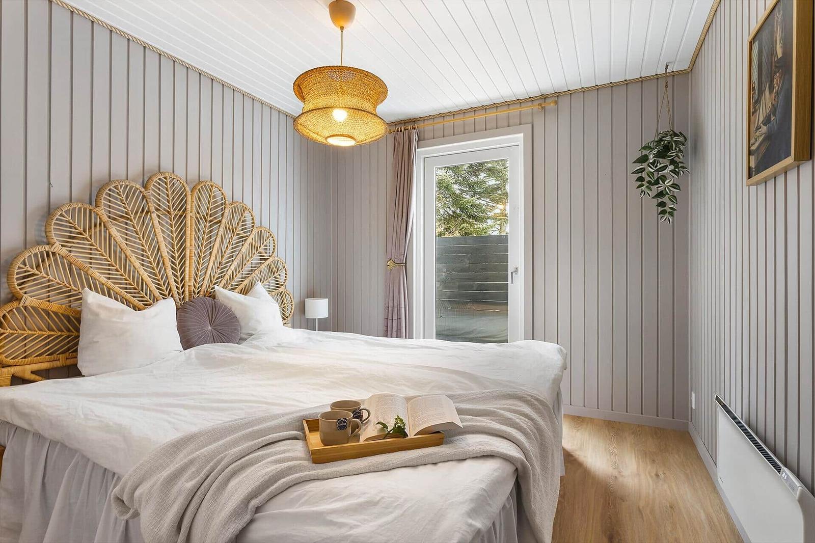 Bedroom with rattan bed and wooden floor. Window with view of garden.