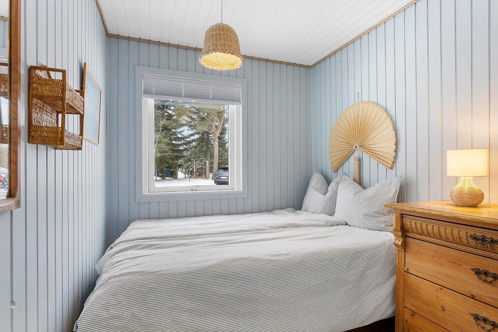Bedroom with bed, dresser, and window view of trees.