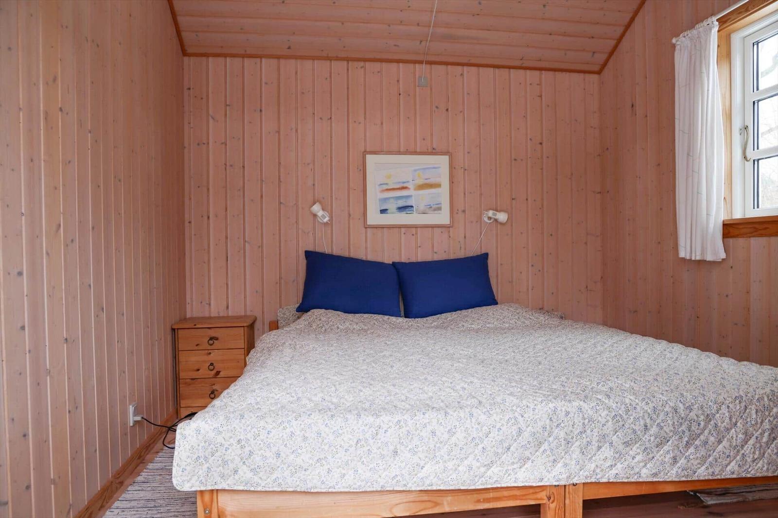 Schlafzimmer mit Holzwand, Bett, Nachttisch und Fenster.