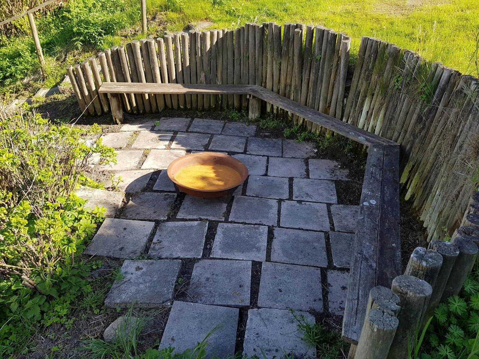 Gartenbereich mit Steinplatten, Holzumrandung und runden Metalltopf.