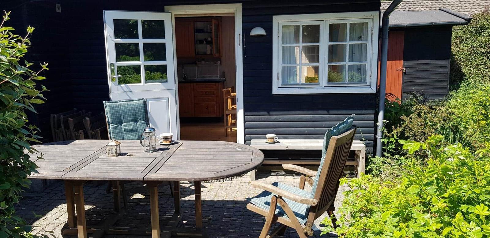 Terrasse mit Tisch, Stühlen und Blick ins Haus. Holztisch, Stühle mit Kissen.