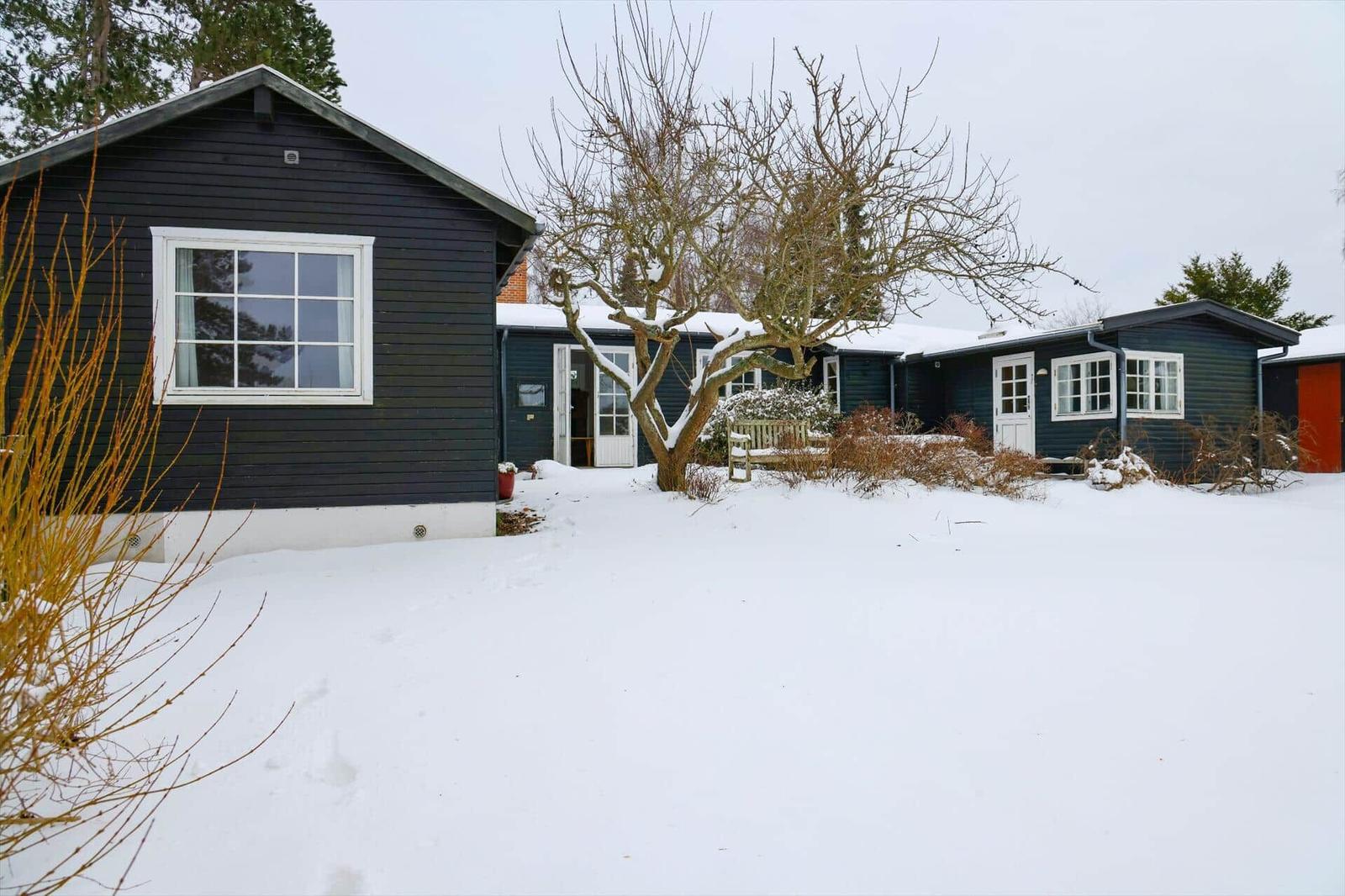 Schwarze Holzhäuser mit weißen Fenstern und Türen im Schnee.