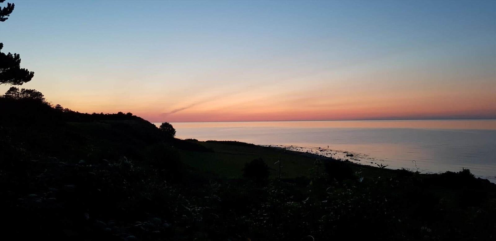 Sonnenuntergang über Meer und Hügeln mit Bäumen im Vordergrund