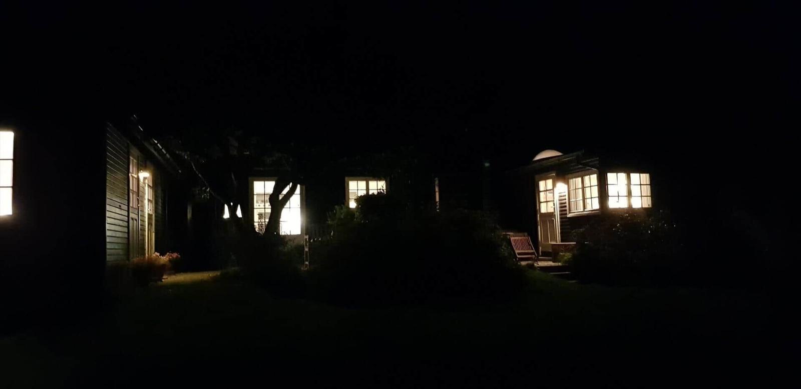 Nachtansicht eines Hauses mit erleuchteten Fenstern und einem Garten