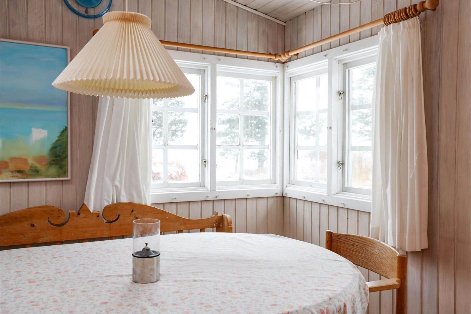 Rundtisch mit Tischdecke und Holzstühle vor Fenstern mit weißen Vorhängen.
