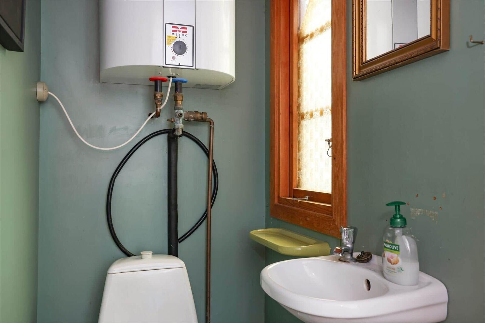 Badezimmer mit Toilette, Waschbecken und Wasserheizer an der Wand.