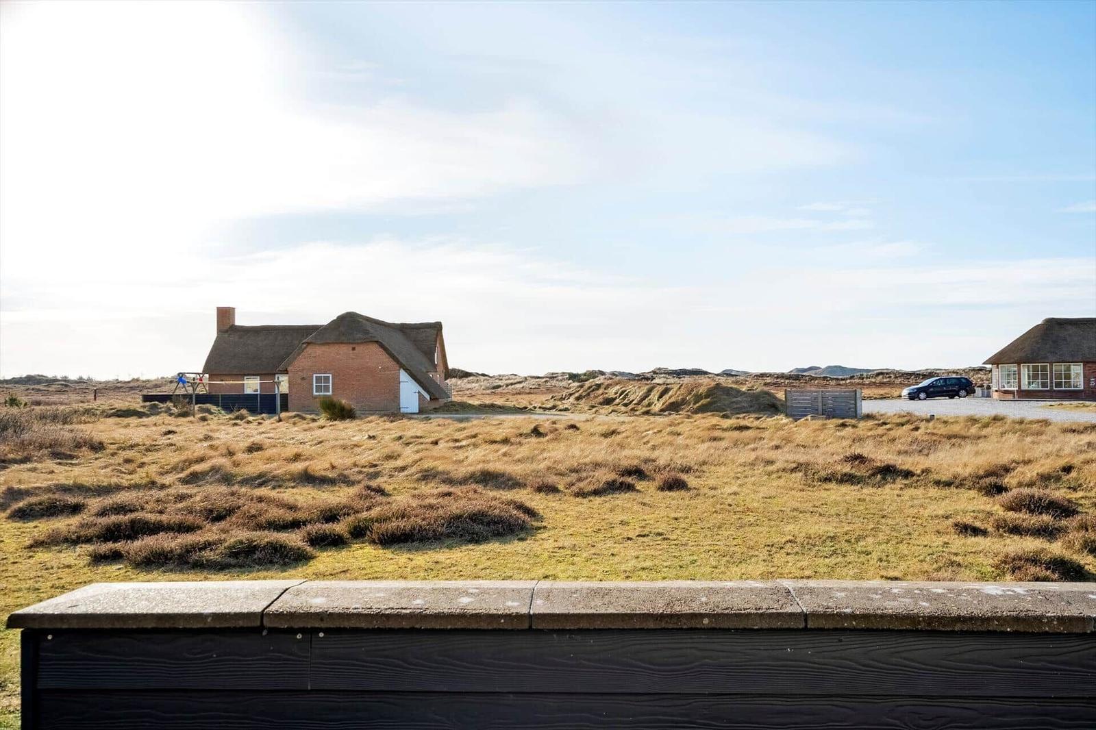Haus mit Strohdach in Dünenlandschaft, Parkplatz und Auto sichtbar.