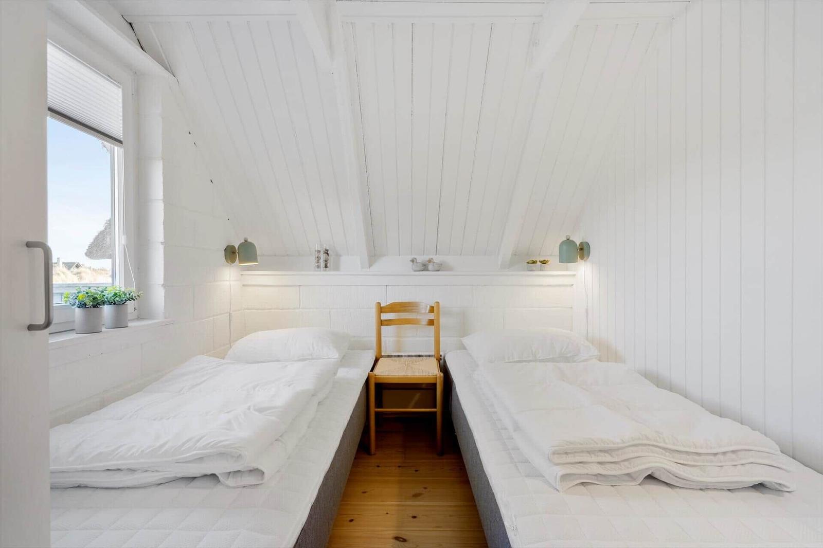 Zwei Betten in einem Dachzimmer mit Holzboden und Fenster.