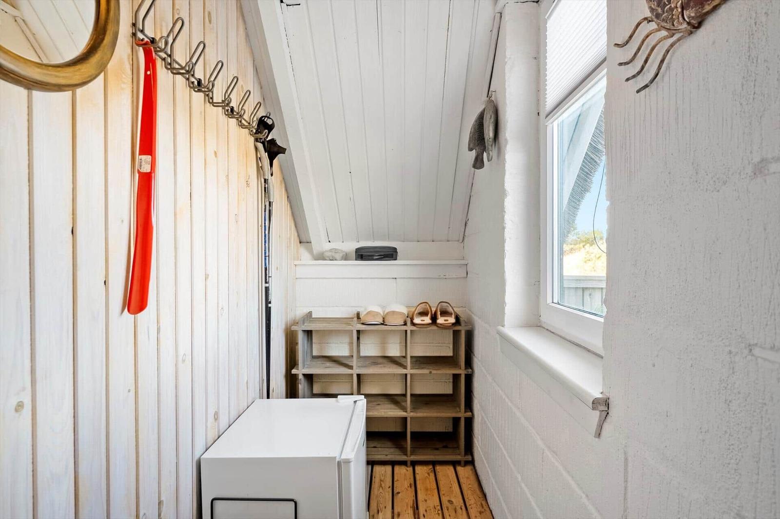 Schlafzimmer mit Dachschräge, Fenster und Schuhschrank. An der Wand hängen Haken und ein Spiegel.