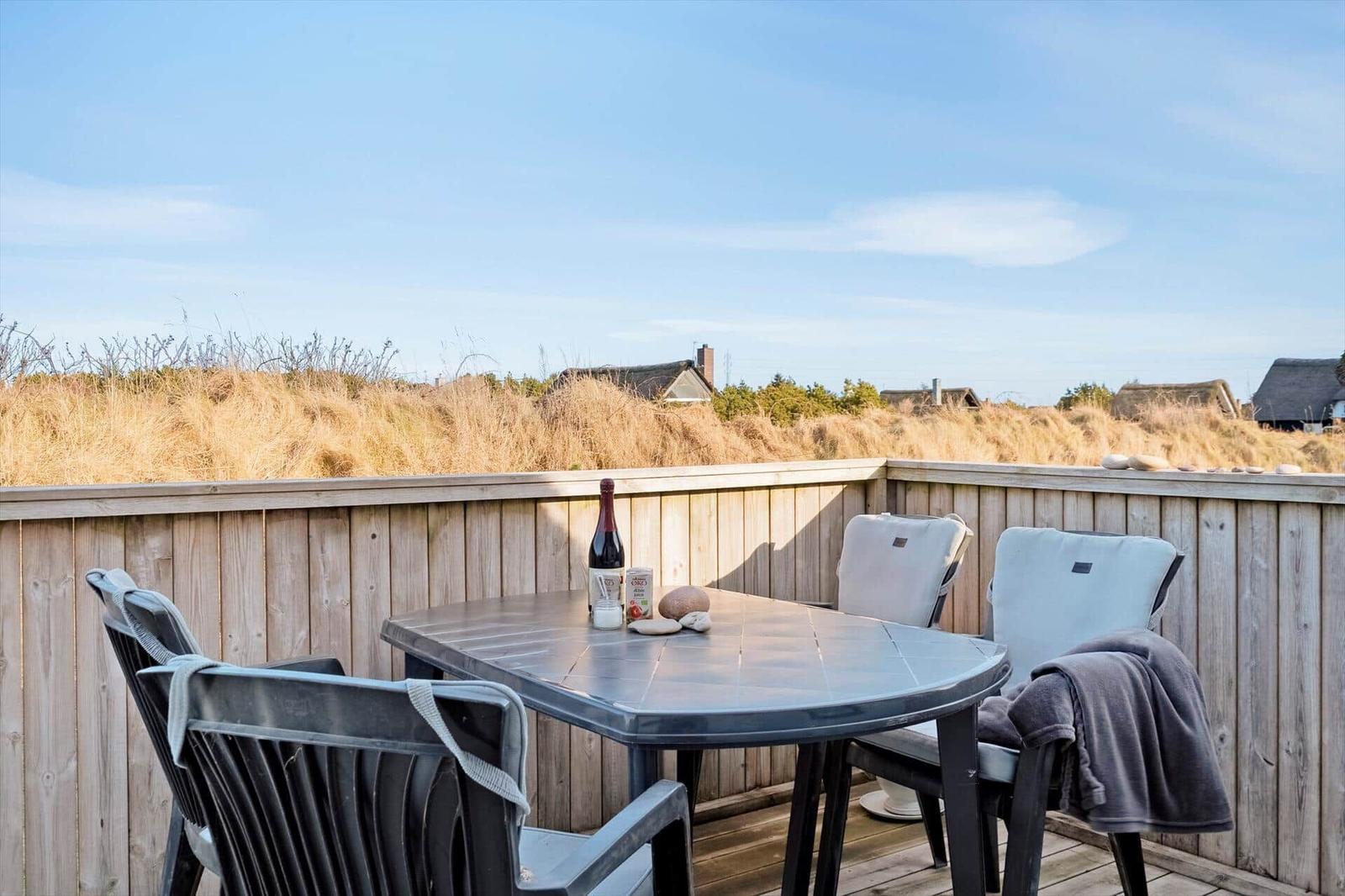 Terrasse mit Tisch und Stühlen, Blick auf Dünen und Häuser im Hintergrund.