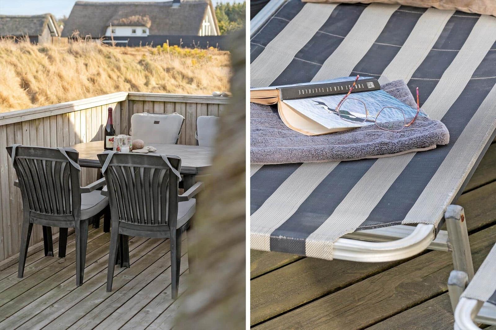 Terrasse mit Tisch und Stühlen, Blick auf Dünen. Liegestuhl mit Buch und Handtuch.
