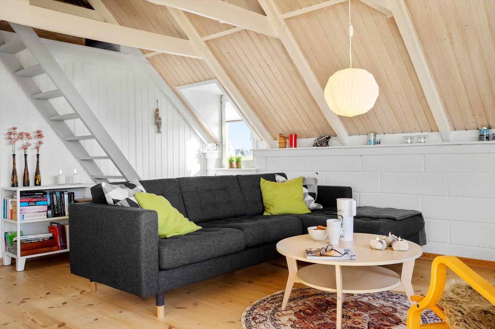 Wohnzimmer mit grafer Sofa, runder Tisch und Holzdecke.