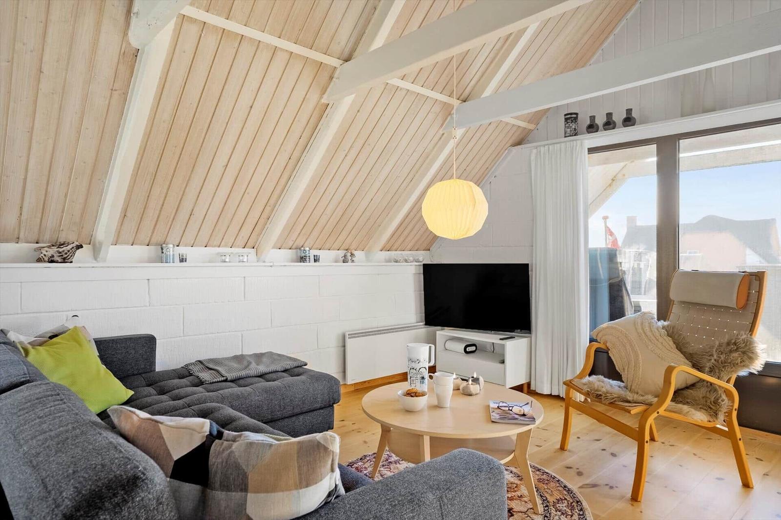 Wohnzimmer mit Sofa, Sessel, TV und Holzboden unter schrägem Dach