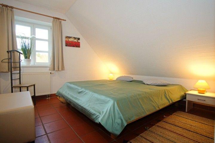 Schlafzimmer mit Dachschrägen, Bett, Nachttisch und Fenster.