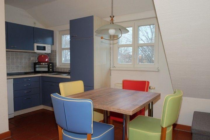 Küche mit Essbereich, blauen Schränken und farbigen Stühlen.