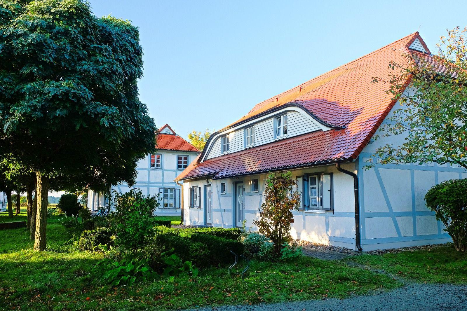 Ein weißes Fachwerkhaus mit rotem Dach und blauen Fensterläden in grüner Umgebung.