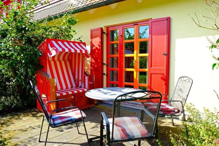 Roter Strandkorb und Sitzgruppe vor gelbem Haus mit roten Fenstern.