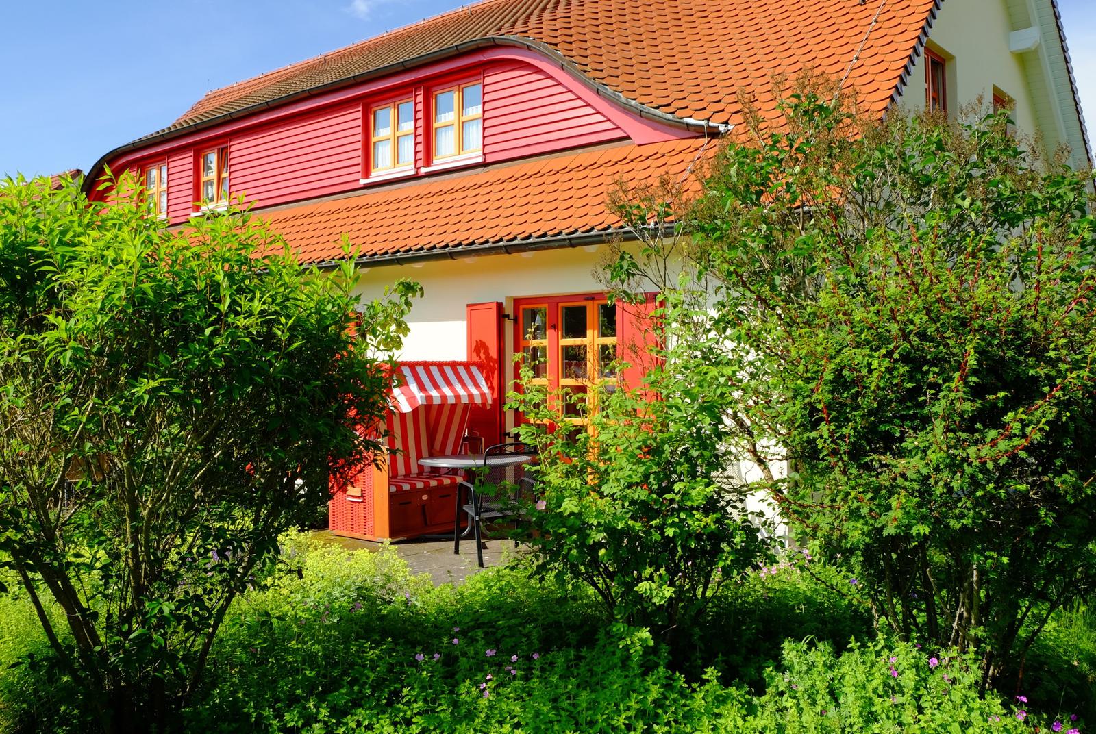 Rotes Haus mit Terrasse und Garten. Rote Fenster und Tür. Strukturierte Dachziegel.
