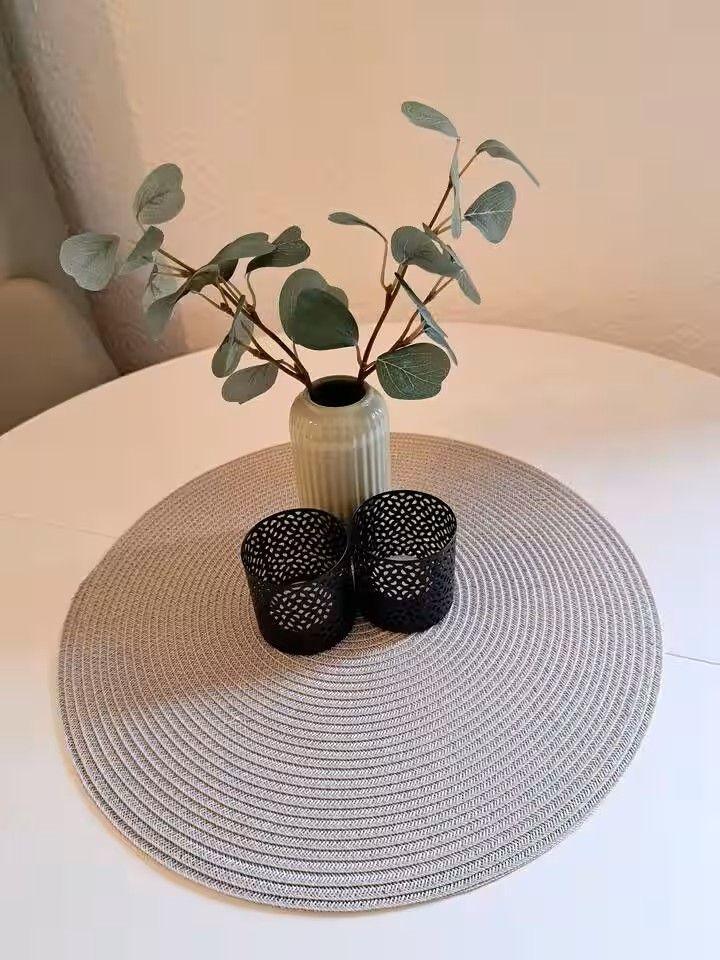 Runde Tischplatte mit runden Untersetzer, Vase und zwei Kerzenhaltern.