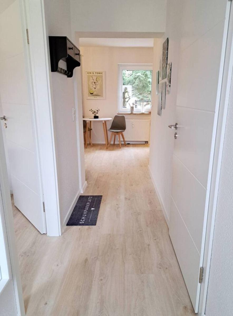 Flur mit Holzboden, Tür zu Wohnzimmer und Schuhmatte mit Schuhparkplatz-Aufschrift.