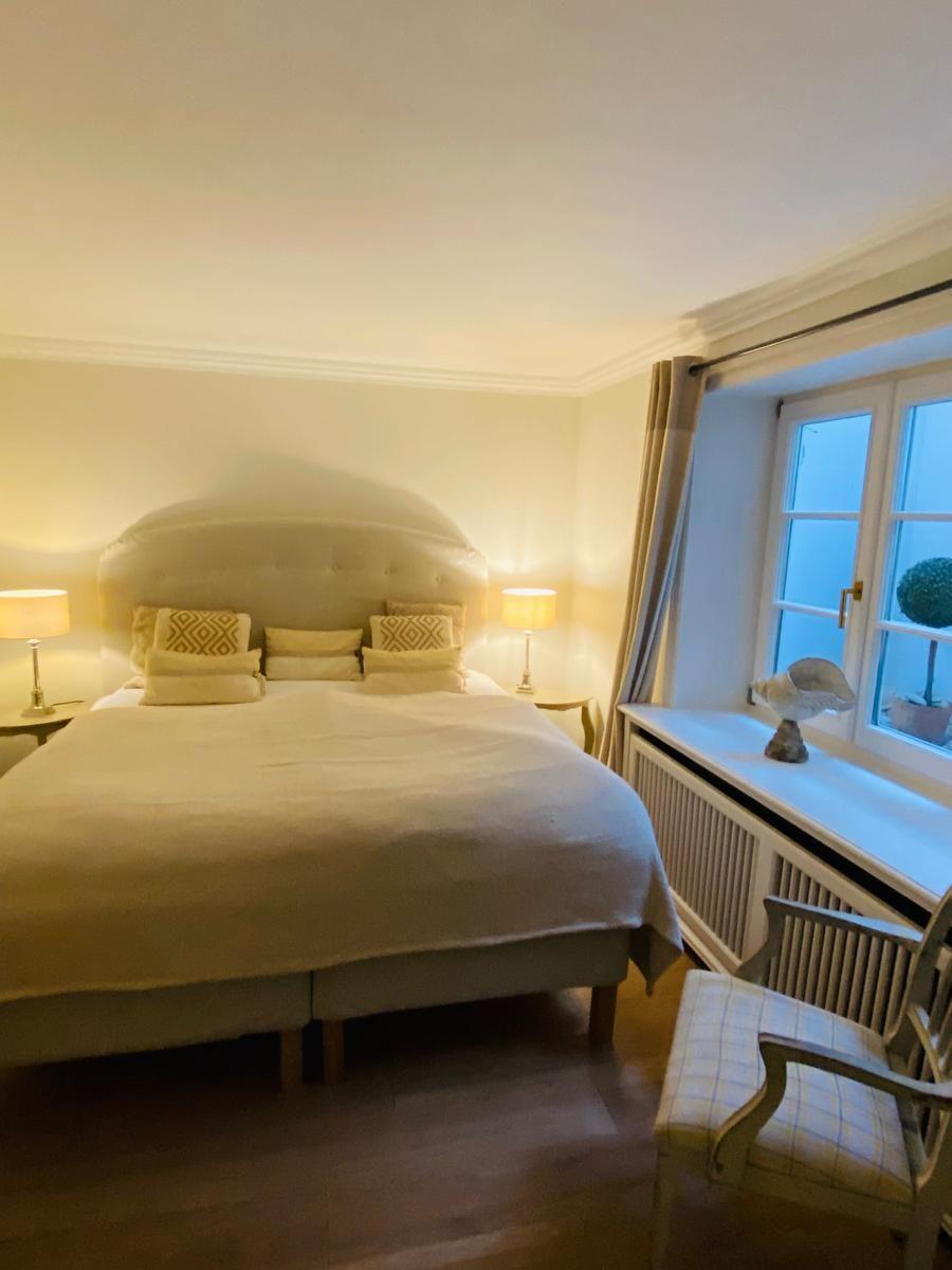 Schlafzimmer mit Bett, zwei Nachttischen und Lampe, Fenster mit Vorhang und Stuhl.