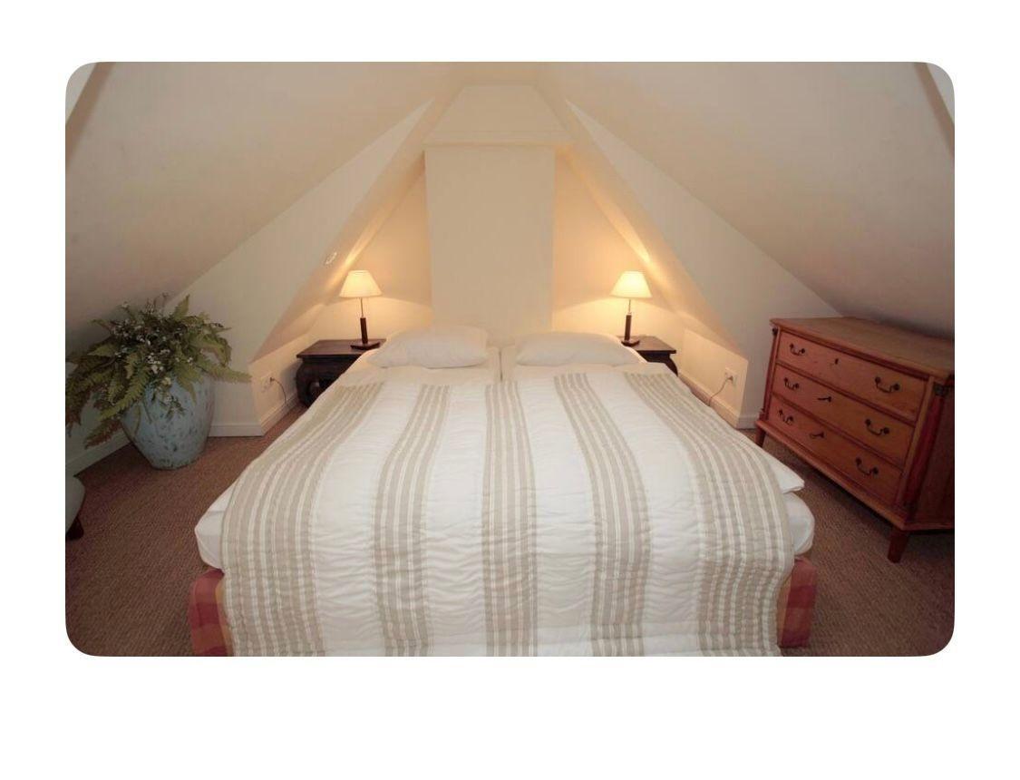 Schlafzimmer mit Doppelbett, Nachttischen und Schrank unter schrägen Dachbalken.