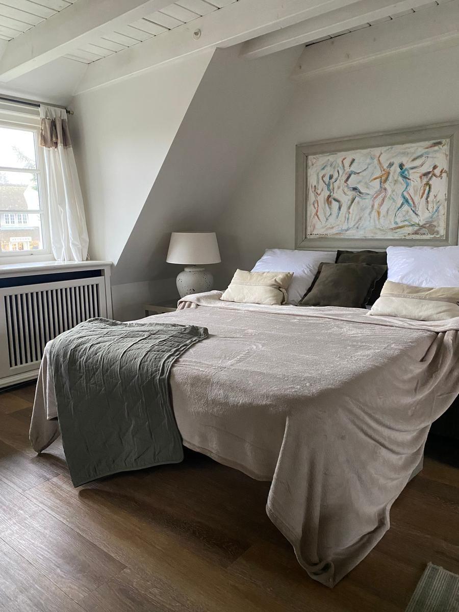 Schlafzimmer mit Dachschrägen, Bett, Fenster und Wandbild.