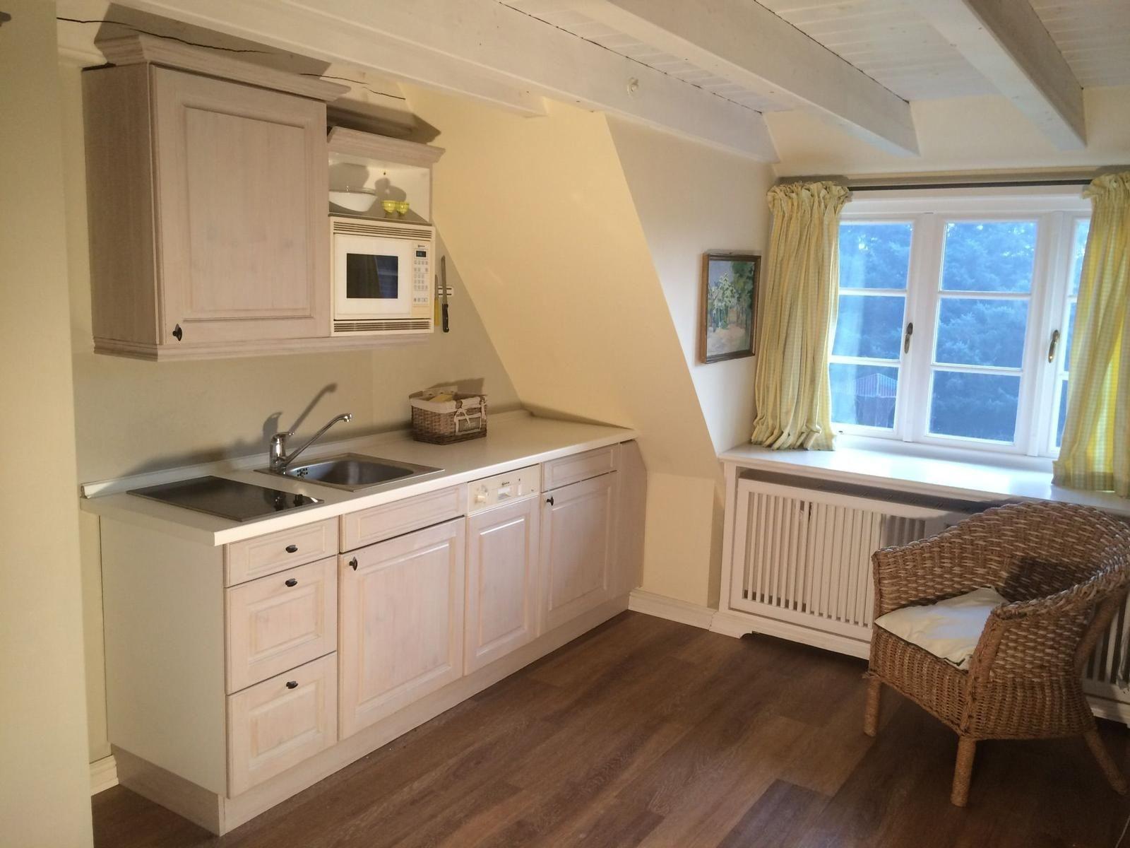 Küche mit Arbeitsplatte, Spüle und Mikrowelle. Fenster mit gelben Vorhängen und Stuhl.