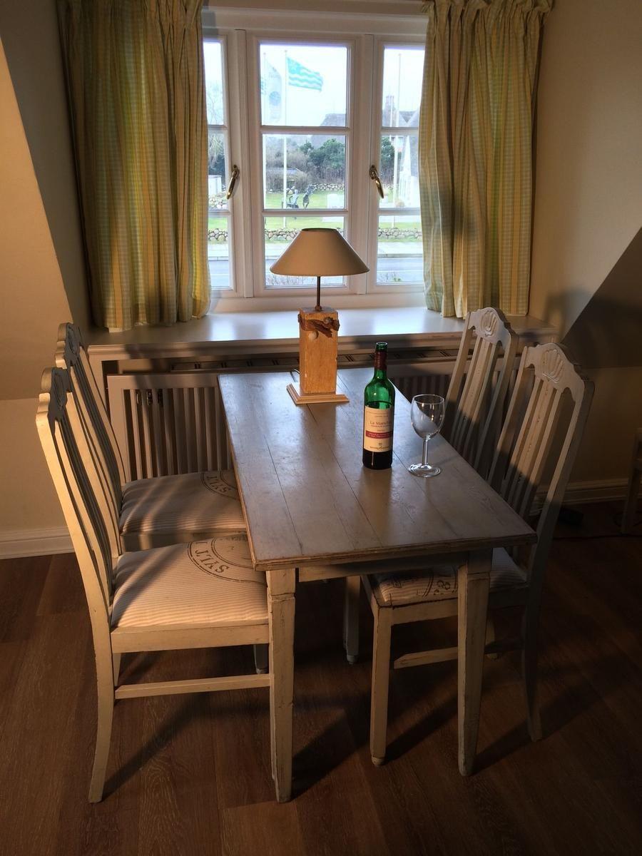 Esszimmer mit Holztisch, vier Stühlen und Fenster mit Gardinen.