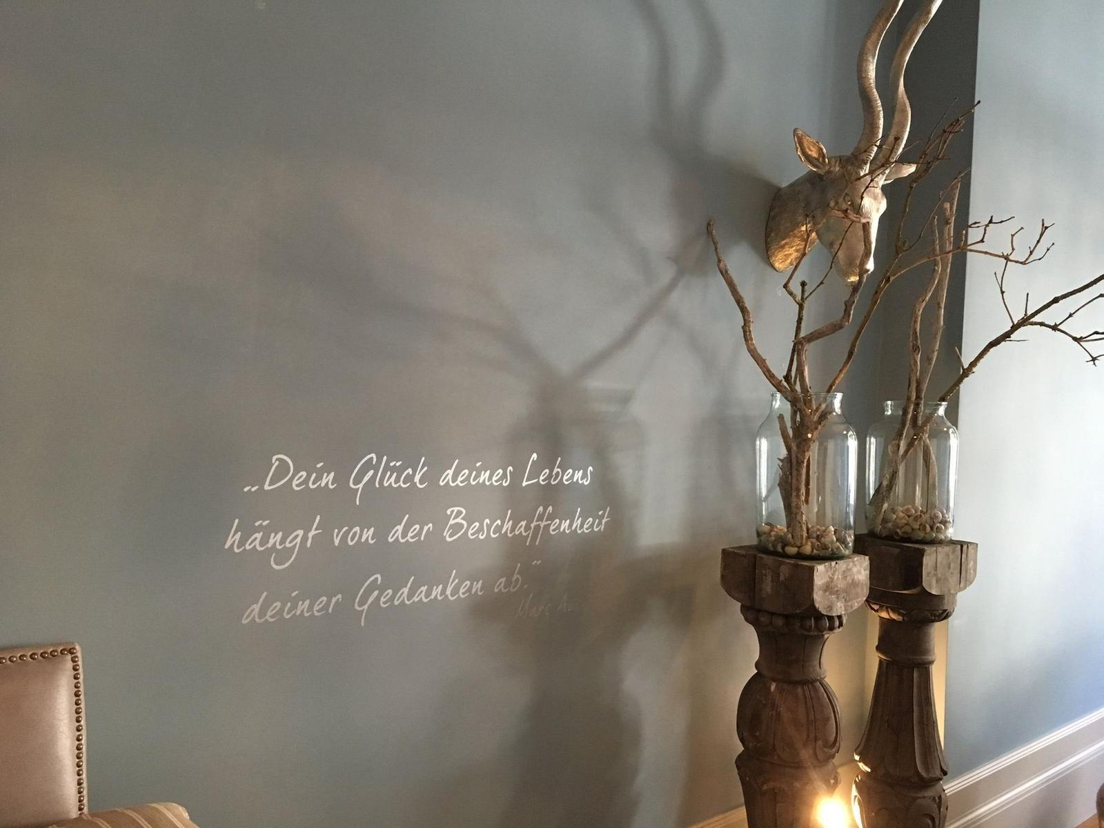 Wand mit Zitat, Rehgeweih und Zweige in Gläsern auf Holzständern