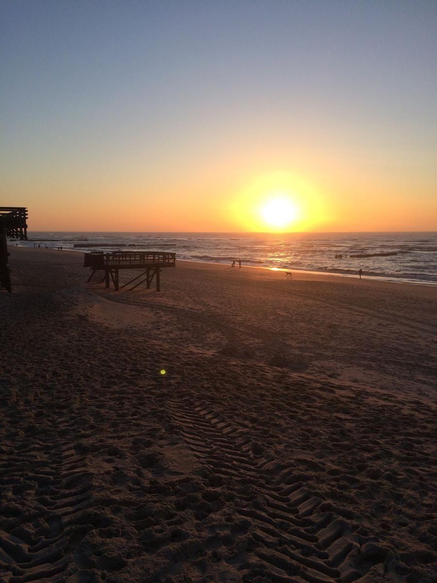 Sonnenuntergang am Strand mit Holzsteg und sanften Wellen.